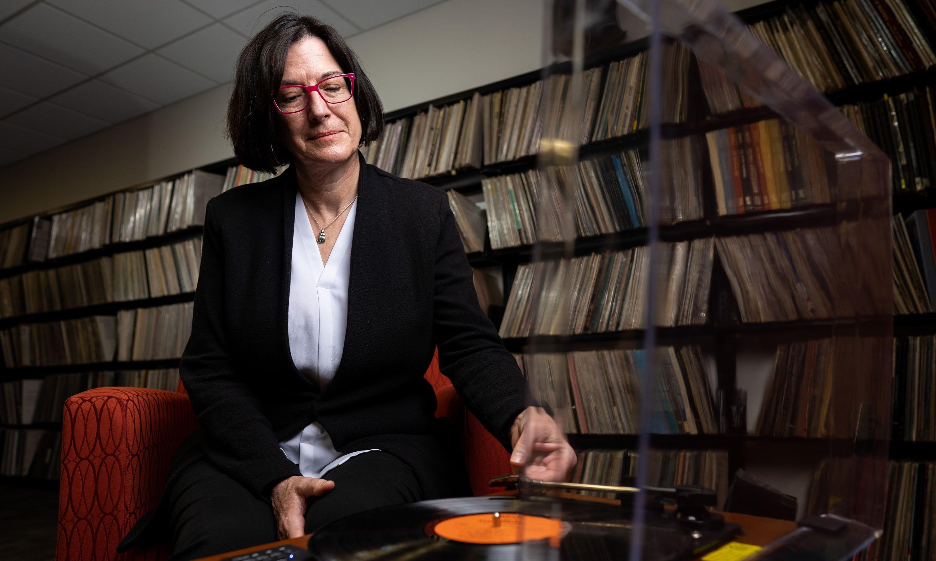 Woman sitting and listening to record with library of record albums in background